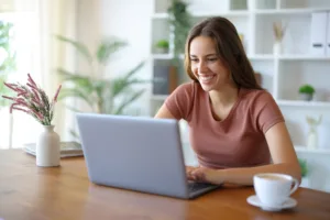 Cum faci rost de bani, atunci când ai nevoie? 9 femeie tanara zambind in fata unui laptop
