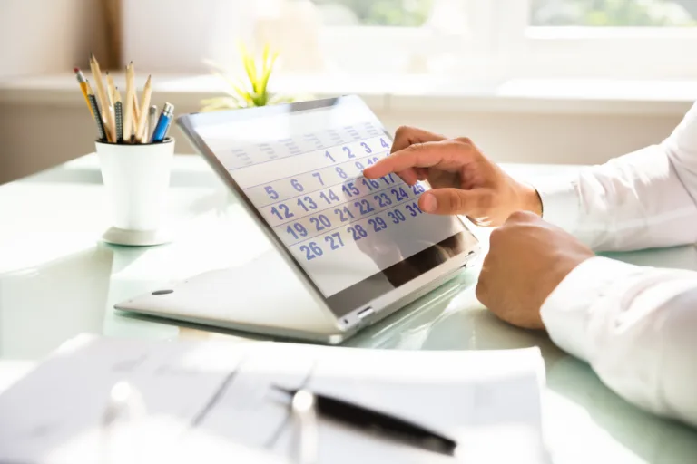 Data scadentă: ce reprezintă și de ce este importantă în gestionarea obligațiilor financiare? 3 barbat in camasa alba la birou utilizand un calendar pe display touch screen cu data scadenta